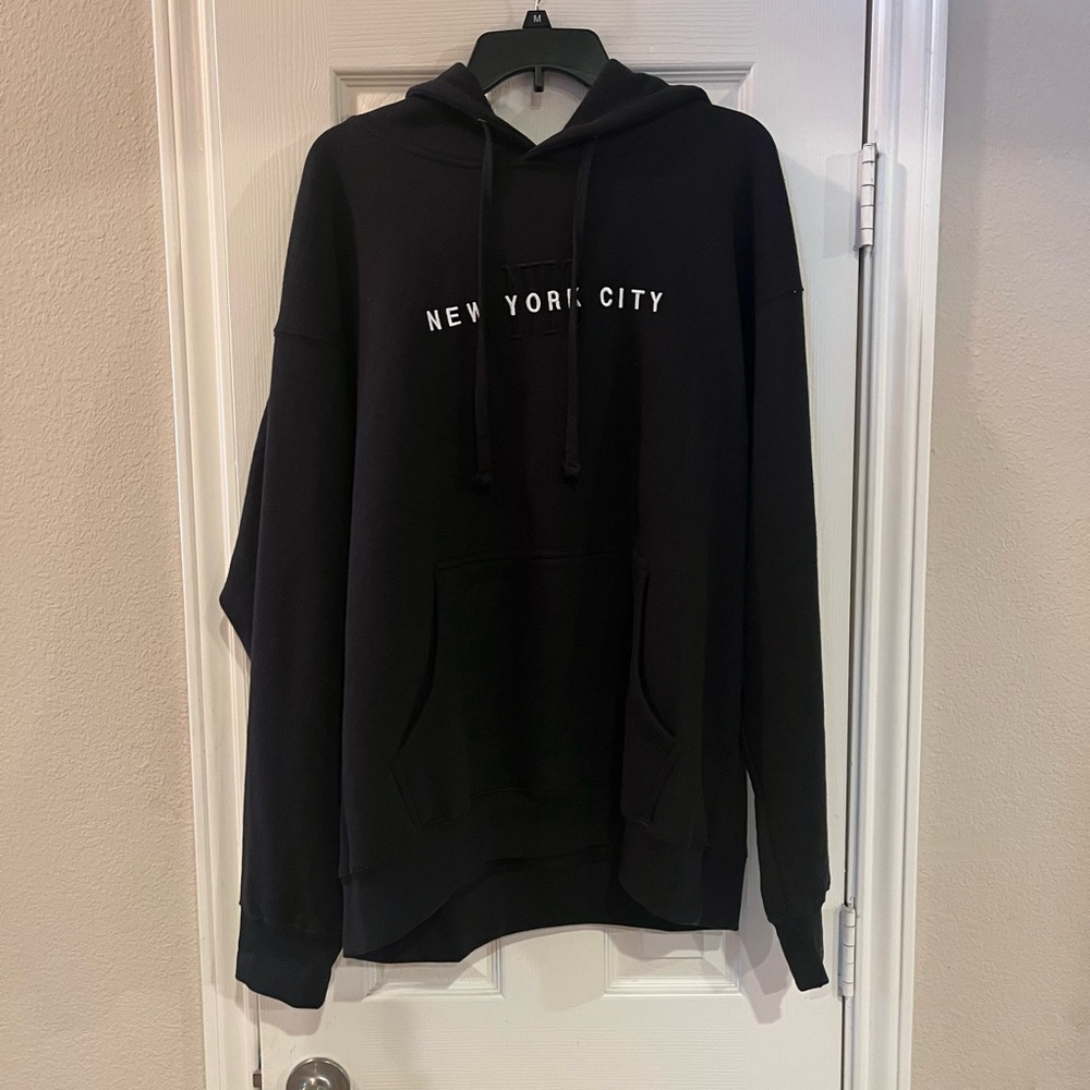 Black hoodie stitched (embroidered) NYC in black. Full words stitched in white.